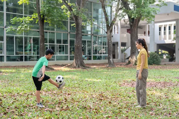 Genç bir çocuk, parkta antrenman yaparak futbol yeteneklerini sergiliyor. Annesi de onu cesaretlendiriyor..