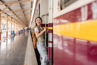 Neşeli bir tebessümle gezgin, ilerideki maceralar için heyecanla yola çıkmaya hazırlanırken tren kapısına tutunur..