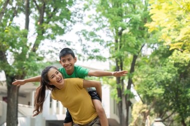 Genç çocuk, aynı gülümsemeyi paylaşan, yakın ve oyuncu ilişkilerini vurgulayan annesi tarafından sırtında taşıdığı neşeyle ışıldıyor..