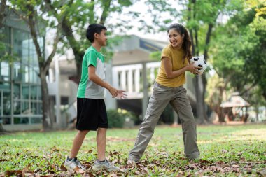 Çocuklar parkta aktif olarak futbol oynuyor, gülümsüyor ve dışarıda sağlıklı aktiviteler yaparken yoldaşlıklarını sergiliyorlar..