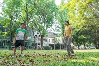 Bir çocuk, arkadaşça bir park atmosferinde bir kadınla uğraşırken futbol yeteneklerini geliştiriyor, takım çalışması ve açık hava eğlencesi sunuyor..