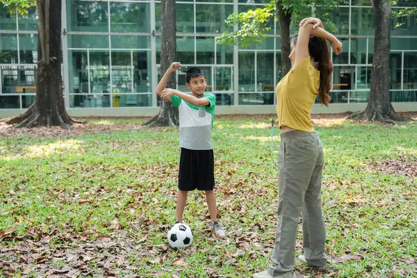 Bir anne ve oğlu yeşil bir tarlada esneme hareketleri yapıyor, birlikte geçirdikleri zamanın tadını çıkarırken spor yapmaya odaklanıyor..