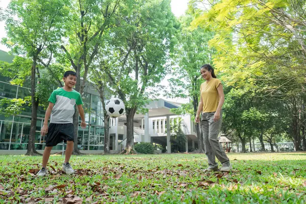Bir çocuk, arkadaşça bir park atmosferinde bir kadınla uğraşırken futbol yeteneklerini geliştiriyor, takım çalışması ve açık hava eğlencesi sunuyor..