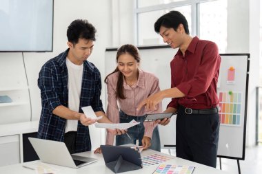 Modern bir ofiste, üç profesyonel tasarım kağıtlarını ve dijital araçları analiz ederek, birlikte yenilikçi çözümler üretme amaçlı işbirlikçi bir ortamı teşvik ederler..