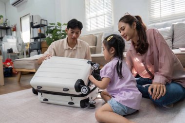 Bir anne ve baba, kızlarıyla oyuncak bir bavulu incelerken eğlenceli etkileşimlerden hoşlanırlar. Konforlu bir ev ortamında aile seyahatleri hazırlıklarının keyfini çıkarırlar..