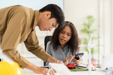 İki takım üyesi, çevre dostu binalar için yenilikçi planlar üzerinde işbirliği yapıyor, fikir alışverişinde bulunuyor ve etkili bir şekilde iletişim kurmak için modeller kullanıyor..