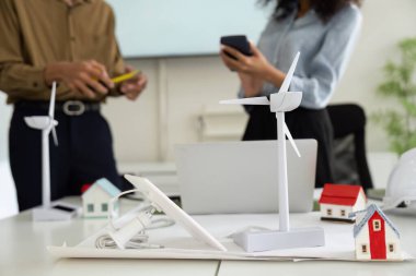 İki profesyonel, rüzgar türbinlerinin ve çevre dostu evlerin minyatür modellerini kullanarak yenilikçi sürdürülebilir enerji çözümleri üzerinde beyin fırtınası yaparak ortak bir toplantı yapıyorlar..