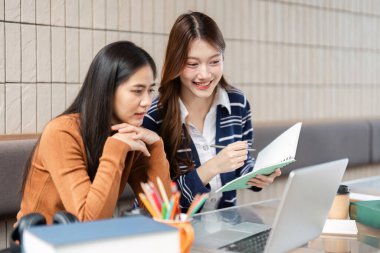 İki arkadaş, sıcak ve davetkar bir çalışma ortamında öğrenme deneyimlerini geliştirmek için bir dizüstü bilgisayar ve not defteri kullanarak görevlerinde işbirliği yapıyorlar..