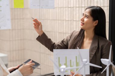 Modern bir ofiste, bir kadın yenilenebilir enerji ile ilgili sürdürülebilirlik verileri sunarak, ESG metriklerinin karar verme mekanizmasındaki önemini vurgular.