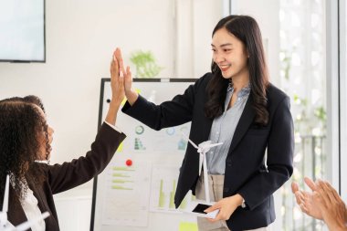 İşbirlikçi bir toplantıda, bir konuşmacı takım üyeleriyle kilometre taşlarını kutluyor, sürdürülebilir enerji projelerindeki başarıları vurguluyor, coşku ve takım çalışmasını teşvik ediyor.