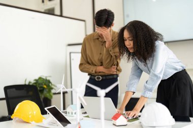 Gösterişli bir ofis ortamında, iki takım üyesi yenilenebilir enerji modellerini analiz ederken, gelecekteki sürdürülebilir çözümlere odaklanıyorlar..