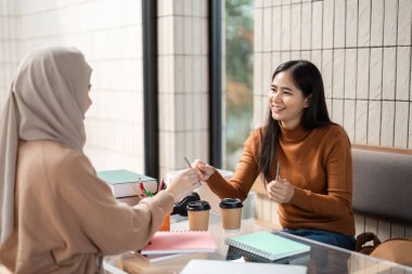 Samimi bir kafe ortasında, iki arkadaş verimli bir çalışma seansına katılır, birlikte kahve içerken notlarını ve fikirlerini paylaşırlar..