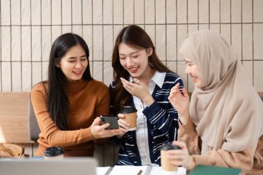 Rahat bir kafe ortamında, üç üniversite arkadaşı, öğrenme deneyimlerini zenginleştirmek için akıllı telefondan bazı içerikleri incelerken aynı kahkahayı paylaşıyorlar..