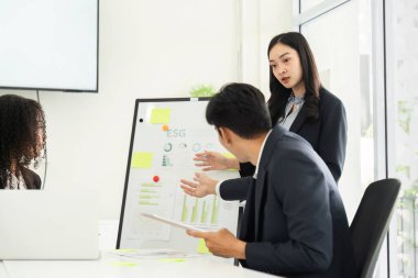 Odaklanmış bir toplantıda, bir ekip üyesi ESG ölçümleri sunarak sürdürülebilirlik yönünde bilgilendirilmiş karar verme mekanizmasını teşvik eder.