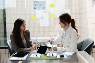 ESG stratejileri hakkında fikir ve görüşleri paylaşan iki kadın, şirketlerinde sürdürülebilirlik çabalarını artırmak için rüzgar enerjisi modellerini inceliyor.