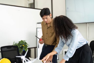 Yenilikçi bir ofiste, bir erkek ve bir kadın birlikte yenilenebilir enerji modellerini analiz eder, işbirliği ve iş dünyasındaki sürdürülebilirliğin önemini vurgularlar..