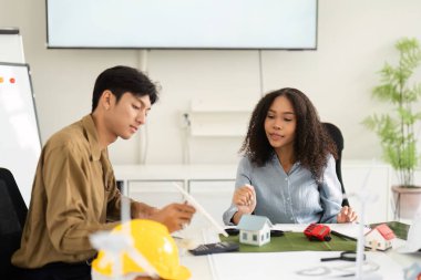 Çağdaş bir ofiste modeller ve araçlarla çevrili sürdürülebilir mimari çözümler hakkında bir tartışmaya giren iki mimar veya mühendis.