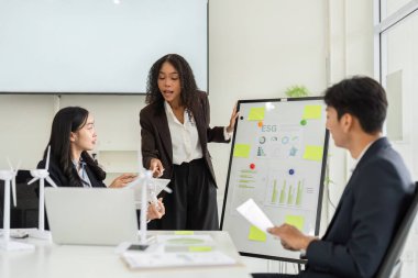 Modern bir ofiste, bir kadın ESG girişimleriyle ilgili önemli ölçüler sunarak, sürdürülebilirlik çabalarını sürdürmek için meslektaşlarıyla açık bir diyalog başlatmaktadır..