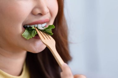 Bu yakın plan, sağlıklı salatasının tadını çıkaran bir kadını yakalıyor. Isırdığı sebzelerin tazeliğini ve canlı renklerini vurguluyor..