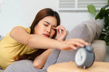 Sıcak bir atmosferde, bir kadın alarmını kapatmaya çalışarak günlük rutininin başlangıcını işaret ediyor. Sahne, uyanmanın zorluklarını somutlaştırıyor..