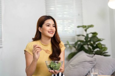 Mutlulukla, bir kadın besleyici bir salata yerken gülümser, sağlıklı alışkanlıkların önemini gösterir ve hayata ve refaha karşı olumlu bir tutum sergiler..