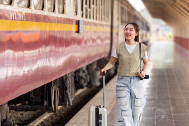 Gülümseyen bir gezgin, bir trene doğru yürürken bavulunu çeker. Yolculuğun ve yeni deneyimlerin heyecanını temsil eden macerası için heyecanlanır..