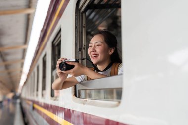 Mutlu bir gezgin, kollarını bir trenin penceresinin önünde dinlendirirken fotoğraf çekmek için kamerasını kullanır. Gezisinde macera duygusunu kucaklar..