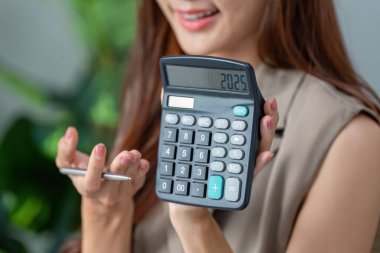 Bir gülümsemeyle, bir kadın 2025 'i gösteren bir hesap makinesini paylaşıyor, gelecek için iyimser finansal tahminlerini sembolize ediyor..