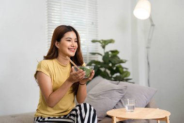 Neşeli bir kadın kanepede oturur, parlak sabah ışığında besleyici bir salatanın tadını çıkararak güne sağlıklı bir başlangıç yapar..