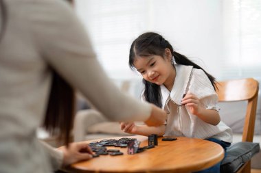 Anne kızına domino taşını uzatır, oyun zamanlarında neşe ve yaratıcılığı ateşler, bakım evindeki aile değerlerini vurgular..