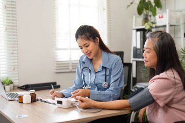 Rutin bir muayene sırasında, hemşire yaşlı bir kadının tansiyonunu ölçer ve rahatlatıcı bir atmosferde tıbbi rehberlik ve destek sunar..