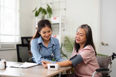 Bir hemşire yaşlı bir hastaya bağlanıyor, kan basıncını ölçüyor ve sıcak bir sağlık ortamında ilaçlarını tartışıyor, sağlığını sağlama alıyor..