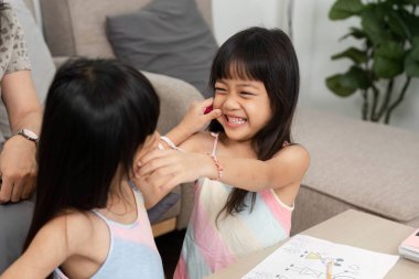 Kız kardeşler yaratıcı faaliyetlerde bulunurken neşeli bir kucaklaşmayı paylaşıyor, oyuncu ilişkilerini ve sanatsal ifadelerini vurguluyorlar..