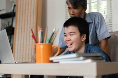 Bir dizüstü bilgisayar kullanarak eğlenceli bir öğrenme deneyimi yaşarken, Down sendromlu bir büyükbaba ve torunu arasında neşeli bir an..