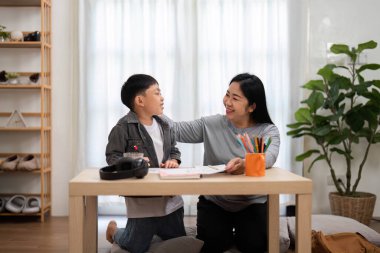 Bir anne ve oğlu, okul ödevleri üzerinde çalışırken keyifli bir anı paylaşıyor, sıcak bir ev ortamında öğrenme sevgisi besliyor..