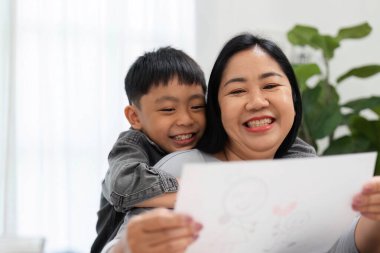 Bir anne, oğlunun renkli çizimlerini göstererek yaratıcılık ve cesaretlendirme yoluyla paylaştıkları bağı vurgulayarak mutlu bir şekilde kucağına alır..