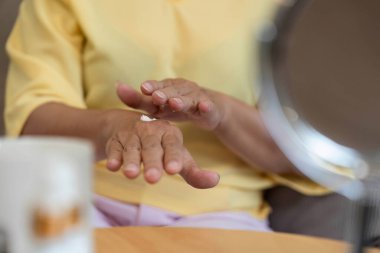 Yaşlı bir kadın ellerine nemlendirici sürerek, her yaşta kendine bakmanın ve güzelliğin önemini vurgular..