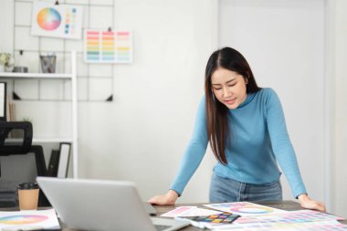 Genç bir kadın masasındaki renk çizelgelerini ve detayları değerlendirir. Projesi için yaratıcı bir şekilde ilham verici seçimler yapar..