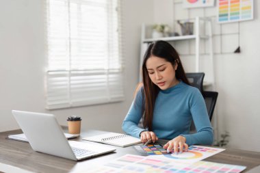 Bir kadın tasarımcı, modern çalışma alanındaki yaratıcı bir projeye hazırlanmak için çeşitli renk örneklerini ve renk paletlerini tutkuyla inceler..