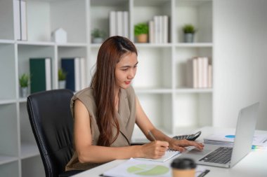 Profesyonel bir ortamda, kendini işine adamış bir iş kadını veri incelemesinden görüşlerini yazar, sunum becerilerini geliştirir ve odaklanmasını sağlar..