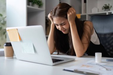 Genç bir iş kadını masasında yorgun ve stresli hissediyor. Çağdaş bir ofis ortamında iş malzemeleriyle çevrili..