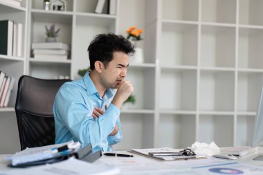 Bir ofis çalışanı masasında oturuyor, soğuk algınlığı yüzünden, etrafı modern ofis ortamında iş malzemeleriyle çevrili..