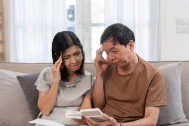 Kanepede oturan yaşlı bir çift, evde faturaları ve mali belgeleri incelerken stresli görünüyorlar..