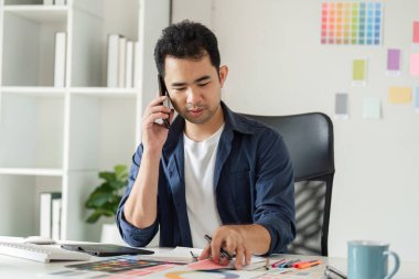 Tasarım araçları ve renk örnekleriyle çevrili bir stüdyo ortamında grafik tasarımcısı, yaratıcı çalışmalara odaklandı.