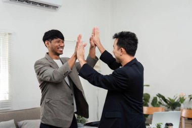 Canlı bir ofis ortamında, iki profesyonel aynı zafer anını paylaşıyor, takım çalışmalarını ve iş dünyasındaki işbirlikçi çabalarının olumlu sonuçlarını sergiliyorlar..