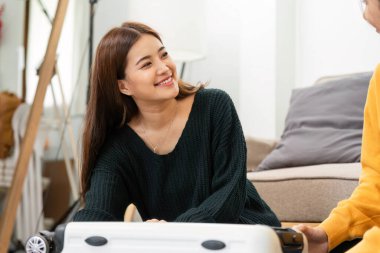 İki genç kadın yerde neşeyle kaynaşıyor, valizlerini seyahat için hazırlıyorlar gülümseme ve kahkahalarla sıcak bir oturma odasında.