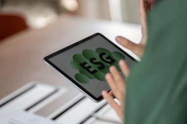 Modern bir ortamda sürdürülebilirlik ve çevre sorumluluğunu vurgulayan ESG kavramını gözler önüne seren dijital tablet tutan bir profesyonel.
