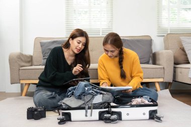 İki kadın, dijital tablette planları tartışırken bir bavula giysilerini koyarak tatile hazırlanıyorlar..