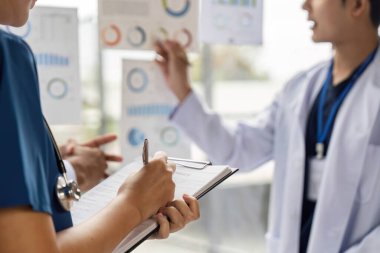 Bir grup doktor çizelgeleri analiz ediyor ve ortak tıbbi ortamda hasta verilerini tartışıyor, ekip çalışması ve hasta bakımını sergiliyor..
