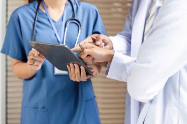 Bir tabletin tıbbi verilerini birlikte inceleyen bir doktor ve hemşire, takım çalışması ve sağlık ortamında odaklanmış iletişimi gösteriyor.